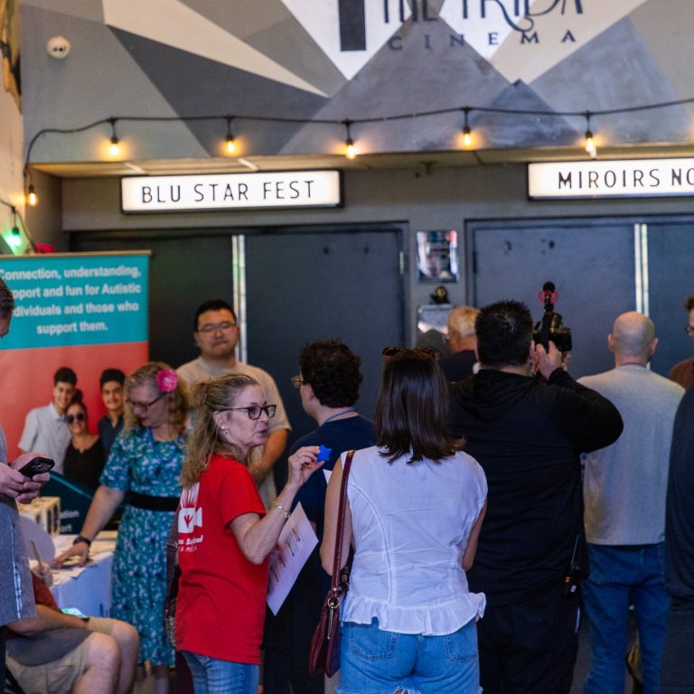 A crowd of attendees gathers in the Frida Cinema lobby under "BLU STAR FEST" and "MIROIRS NO 3" marquee signs, with string lights and colorful murals decorating the walls.
